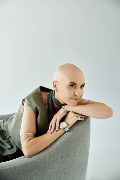 Лысая женщина обнимает свою уникальность, элегантно отдыхая на современном стуле, излучая силу.