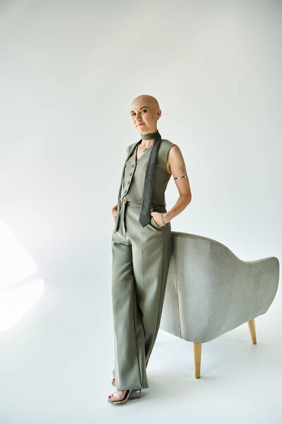 Молодая лысая женщина излучает уверенность, позируя в шикарном современном внутреннем пространстве.