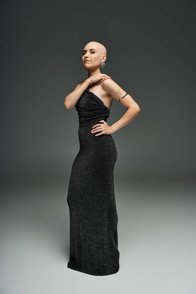 A young bald woman confidently showcases her elegance in a stylish black gown, radiating beauty.