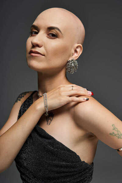 Молодая лысая женщина демонстрирует свою красоту, одетая в элегантный наряд и уникальные украшения с уверенностью.