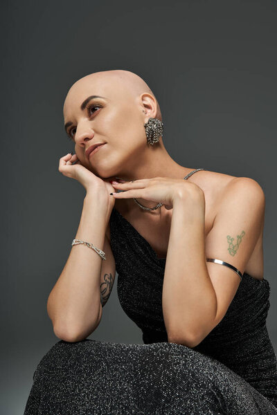 A young bald woman with alopecia elegantly poses in a black dress, showcasing confidence and grace.