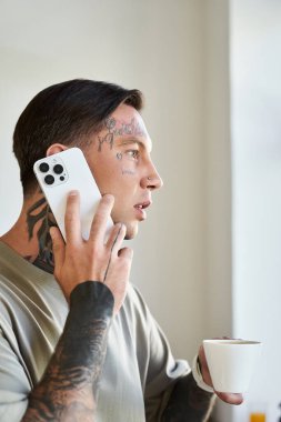 Genç bir adam, elinde bir fincan kahveyle telefonuyla rahat bir ortam yaratıyor..