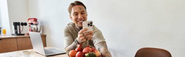 Yakışıklı genç bir adam canlı meyvelerle çevrili neşeli bir selfie çekerken gülümsüyor..