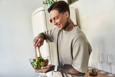 Kendinden emin genç bir adam cam bir kasede canlı bir salata karıştırır, evde yemek pişirmekten zevk alır..