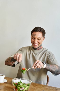 Genç bir adam evinde kahvesini yudumlarken neşeyle taze bir salata hazırlar..
