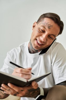 Genç bir adam, bir telefon görüşmesi ve not alma arasında birden fazla iş yapan fikirlerini yazarken gülümsüyor..