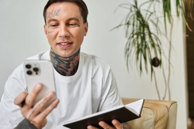 Genç bir adam akıllı telefonuyla gülümseyerek ve rahat bir şekilde etkileşime geçerek evde bir andan zevk alır..