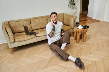 A young man sits on the floor, chatting on the phone in a cozy atmosphere. clipart