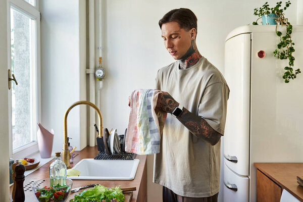 A handsome young man is engaged in meal prep, thoughtfully drying a dishcloth in a cozy kitchen.