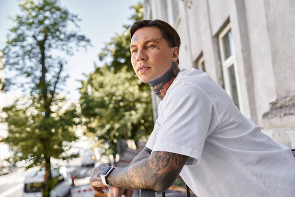 Он небрежно наклоняется на балкон, впитывая солнце и любуясь оживленной улицей под ним..