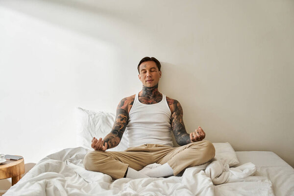 Красивый молодой человек сидит со скрещенными ногами на кровати, глубоко погруженный в медитацию..