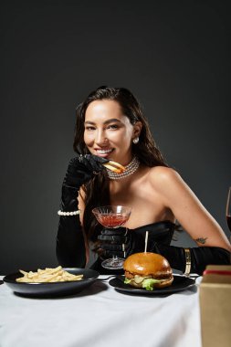 The beautiful woman indulges in gourmet fast food while exuding elegance and charm. clipart