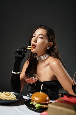Şık giyinmiş genç bir kadın kokteyl yudumlarken gurme fast food yiyor..