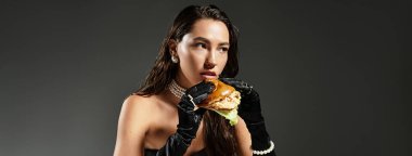Tarz sahibi genç bir kadın gurme burgerin tadını çıkarıyor, sofistike ve zevkli bir şekilde harmanlıyor..