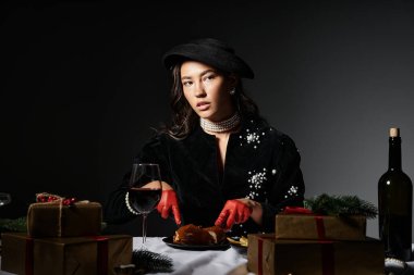 In an elegant setting, a beautiful woman in luxury attire admires her festive dish and gifts. clipart