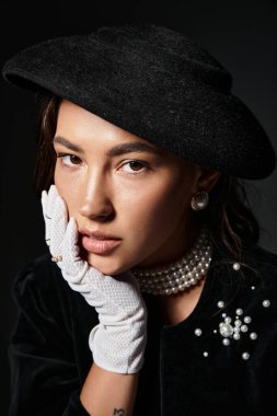 Genç bir kadın, siyah bir şapka ve ince inci aksesuarlarla zarafet sergiliyor, derin düşüncelere dalmış..