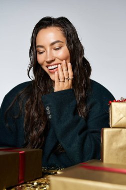 A radiant young woman enjoys a moment of joy surrounded by stylishly wrapped gifts. clipart