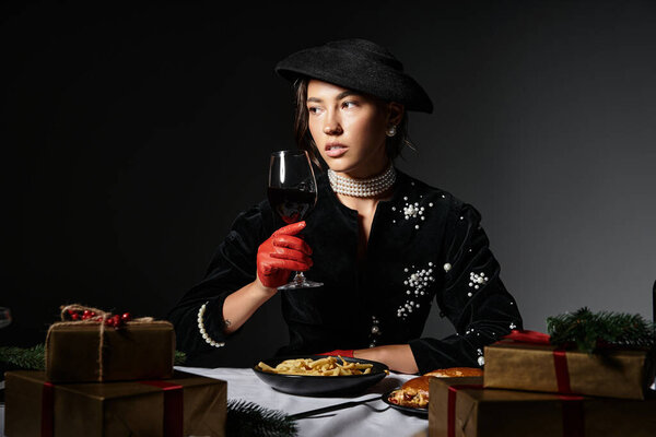 The elegant woman in luxurious attire savors a festive meal with wine in hand.