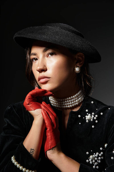 A young woman exudes elegance with pearls and red gloves, captured in a striking pose.