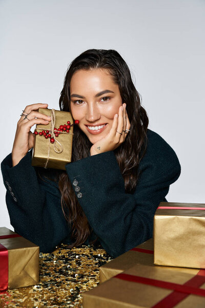 A sophisticated young woman, dressed elegantly, smiles while holding a beautifully wrapped gift.