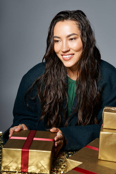 A sophisticated woman with wet hair smiles as she arranges golden presents for a special occasion.