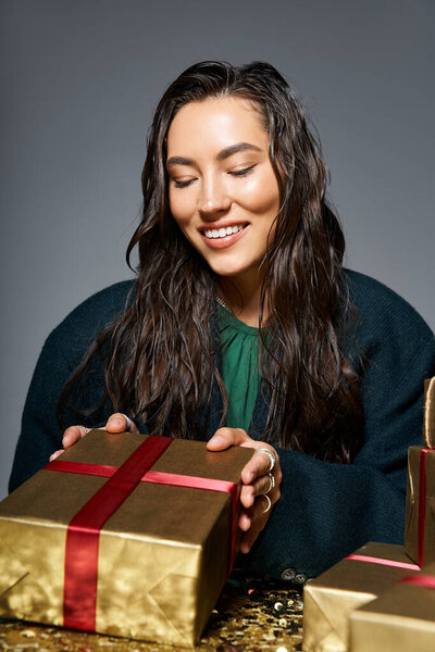 An elegant woman smiles as she opens a lovely present amid festive surroundings.