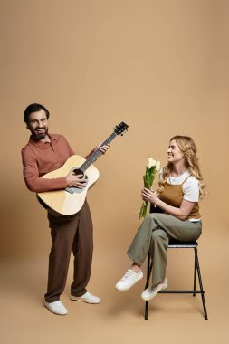 Orta yaşlı bir adam gitar çalarken neşeli bir kadın elinde çiçeklerle anın tadını çıkarıyor..