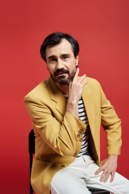 Sarı ceketli orta yaşlı bir adam nazikçe çenesine dokunuyor, derin düşüncelere dalmış..