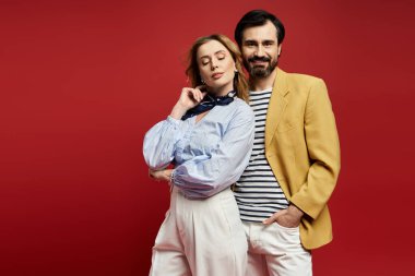 Orta yaşlı bir çift şık kıyafetler içinde, cesur kırmızı bir zemin ile gösteriş yapar..