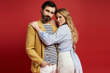 Bir çift düşünceli bir şekilde sarılıyor, moda tercihlerini sıcak kırmızı bir arka planla sergiliyor..