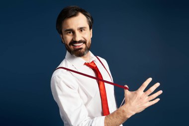 Neşeli orta yaşlı bir adam kendine güvenerek gülümsüyor, kırmızı kravatıyla oyuncu bir poz veriyor..