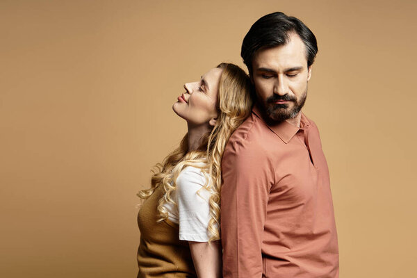 Пара средних лет стоит спиной к спине, излучая тепло и связь в уютной обстановке.