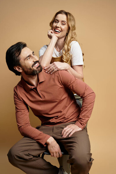 A cheerful middle aged couple enjoys a playful moment against a soft, warm backdrop.