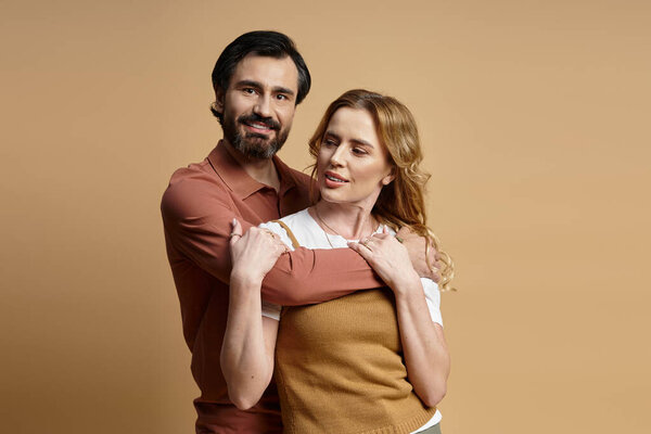 Пара средних лет нежно обнимается в уютной студии, наполненной теплыми красками..