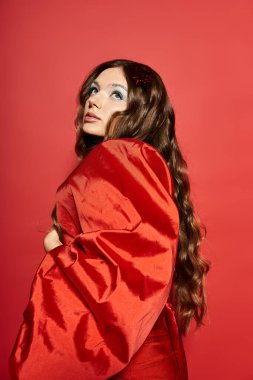 Güzel genç bir kadın, çarpıcı kırmızı bir elbise içinde, zarafet saçarak arkasına bakar..