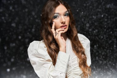 Dalgalı saçları olan çarpıcı bir genç kadın, kar yağışında şık bir kıyafet ve çarpıcı bir makyaj sergiliyor..