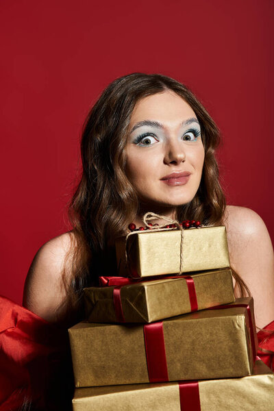 Восхитительная молодая женщина позирует со стопкой завернутых подарков на ярком красном фоне.
