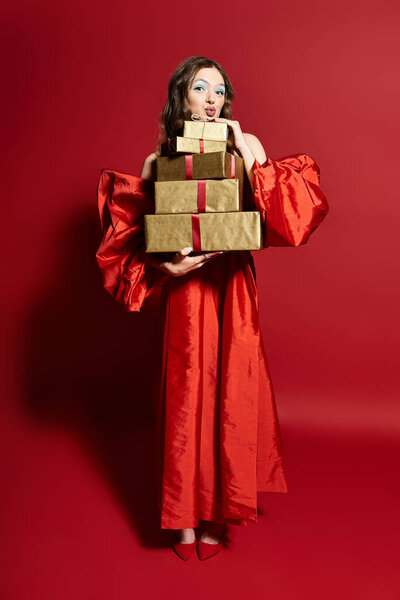 Красивая молодая женщина в красном платье с радостью позирует с несколькими элегантно завернутыми подарками.