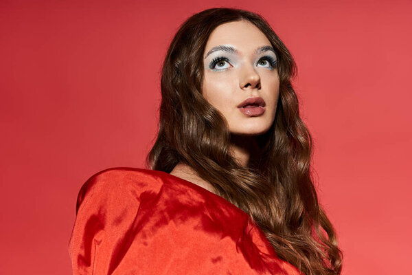 Красивая молодая женщина вдумчиво смотрит вверх, одетая в ярко-красный наряд.