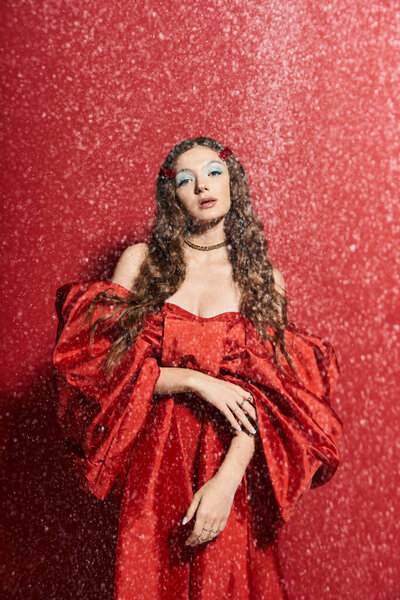 Красивая молодая женщина стоит изящно, украшенная в ярко-красное платье с снежной атмосферой.