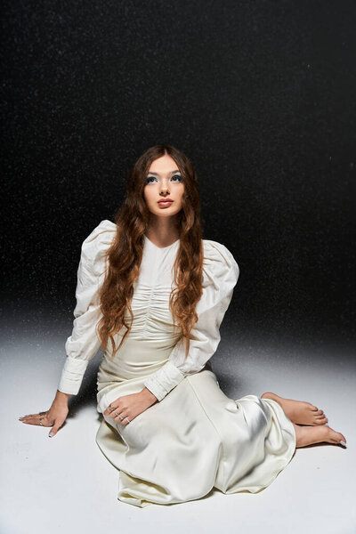 Изящная молодая женщина в белом платье сидит элегантно, излучая красоту.