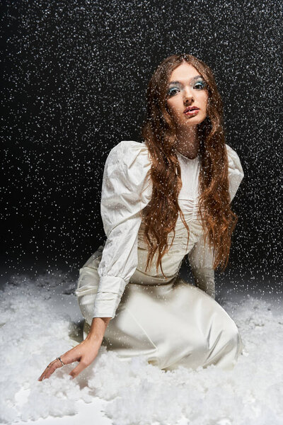 Молодая женщина в элегантной белой одежде преклоняет колени в снежной обстановке, излучающей спокойствие и красоту.