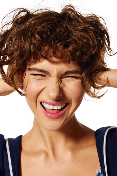 A young woman with curly hair showcases her joyful spirit while playfully covering her ears.