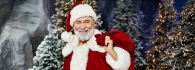 Neşeli bir gülümsemesi olan neşeli bir Noel Baba, karlı bir tatil ortamında kırmızı bir çanta tutuyor..