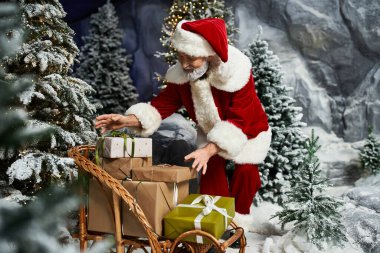 Noel Baba, karla kaplı ağaçlarla çevrili bir kızakta renkli hediyeler hazırlar..
