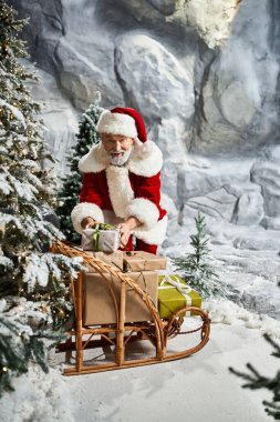 Neşeli Noel Baba kızağında karla kaplı ağaçlarla renkli hediyeler organize eder..