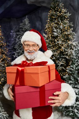 Neşeli bir Noel Baba, kışın neşe içinde neşeli ağaçlarla çevrili canlı hediye kutuları tutar..