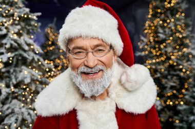 Klasik bir Noel Baba kostümüyle neşeli bir figür, ışıl ışıl ağaçlarla çevrili tatil neşesini paylaşıyor..