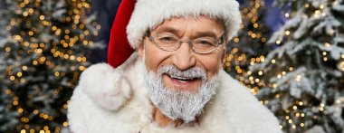 Neşeli bir Noel Baba, ışıl ışıl ağaçlarla çevrili sıcak bir gülümsemeyle bayram neşesini yayar..