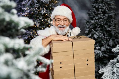 Noel Baba kışın harikalar diyarında bir yığın hediye kutusunu taşırken ışıl ışıl gülümser.